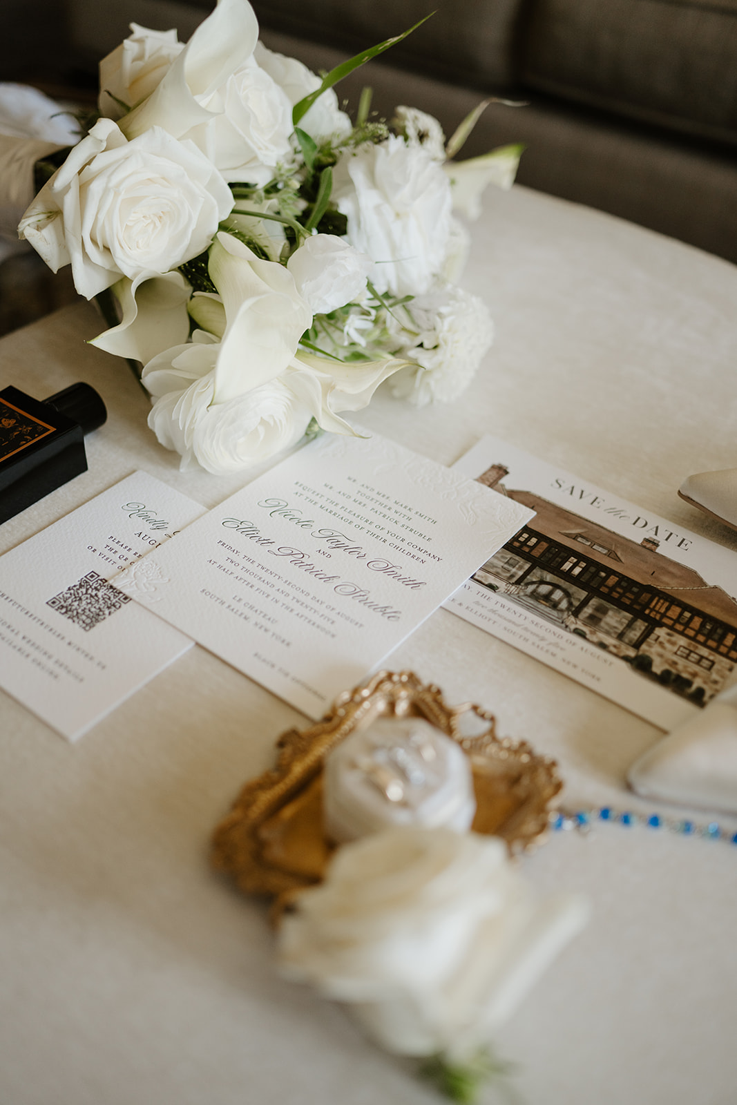 Elegant wedding invitation suite arranged flat lay with white roses, wedding rings, and a save the date card.